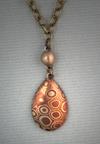 Pear shaped pendant of bronze & copper Mokume Gane. Measures 1/2" w x 1 12" h. Hangs on an antiqued bronze 18" to 22" adjustable chain.