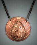 Water Drop Mokume Gane Pendant;  Dia. = 1 5/8;   Hand-sculpted oval and domed Mokume Gane pendant made up of copper, bronze, and steel, on a backing of Copper upon which are a ripple of bronze inlaid circular lines.  Hangs on a 19” to 21” antiqued bronze adjustable chain.